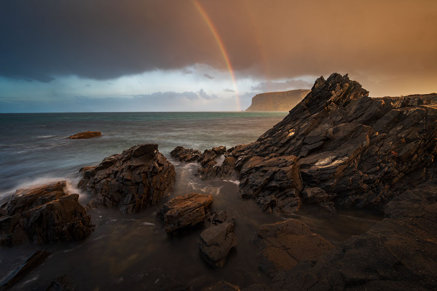 Rainbow appearing over a rocky coast as rain clears